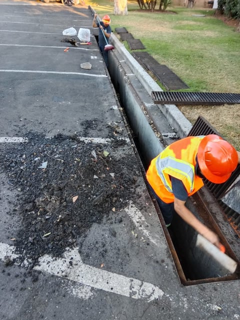 Construction worker in safety vest and hard hat working in drainage system along asphalt road