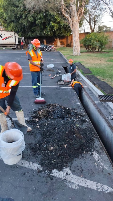 Construction workers in safety vests and hard hats performing road maintenance work with asphalt and drainage infrastructure