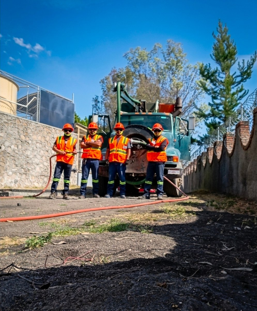 Four construction workers in safety vests standing by asphalt paving machinery on a sunny day at a work site