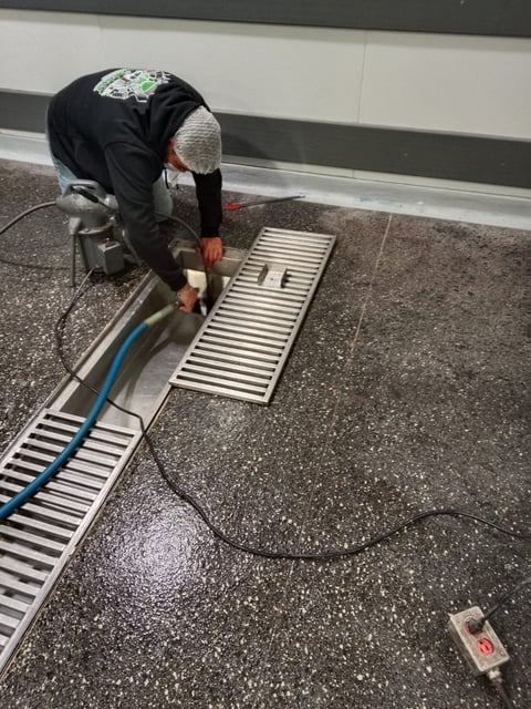 Worker installing metal floor grates with power drill on commercial epoxy floor